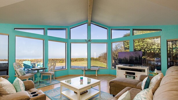 A spacious living room with large windows, a television, and comfortable seating.