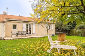 A house with a tiled roof, a patio with a table and chairs, and a lawn with scattered leaves.
