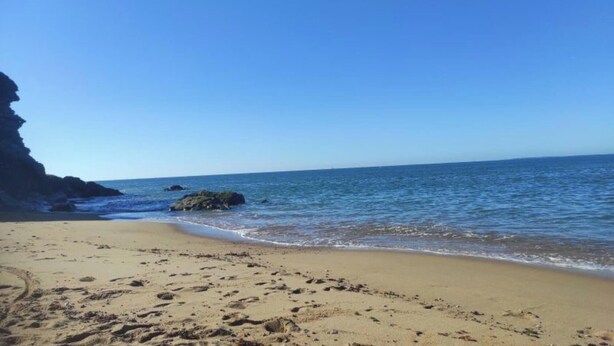 Une plage avec un ciel dégagé, une eau calme et des affleurements rocheux.