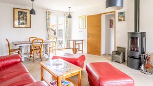 Un salon avec un canapé rouge, une table en bois, une cheminée et un coin repas comprenant des chaises et une table.