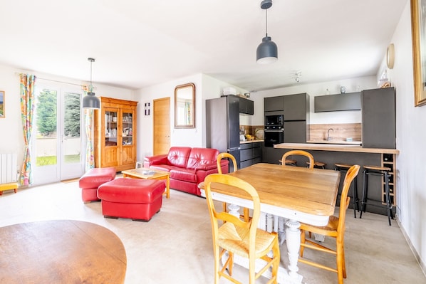 A modern kitchen with dark cabinets, a wooden dining table, and a red leather sofa.