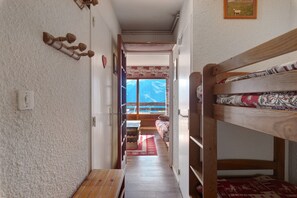 A narrow hallway with a bunk bed on the right, a wooden bench, and a door leading to a room with a view of mountains. - Studio 'Pathabac' with Mountain View and Balcony (Auris)