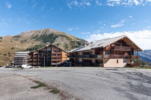 A multi-story wooden building with balconies, a parking area, and a mountainous backdrop. - Studio 'Pathabac' with Mountain View and Balcony (Auris)