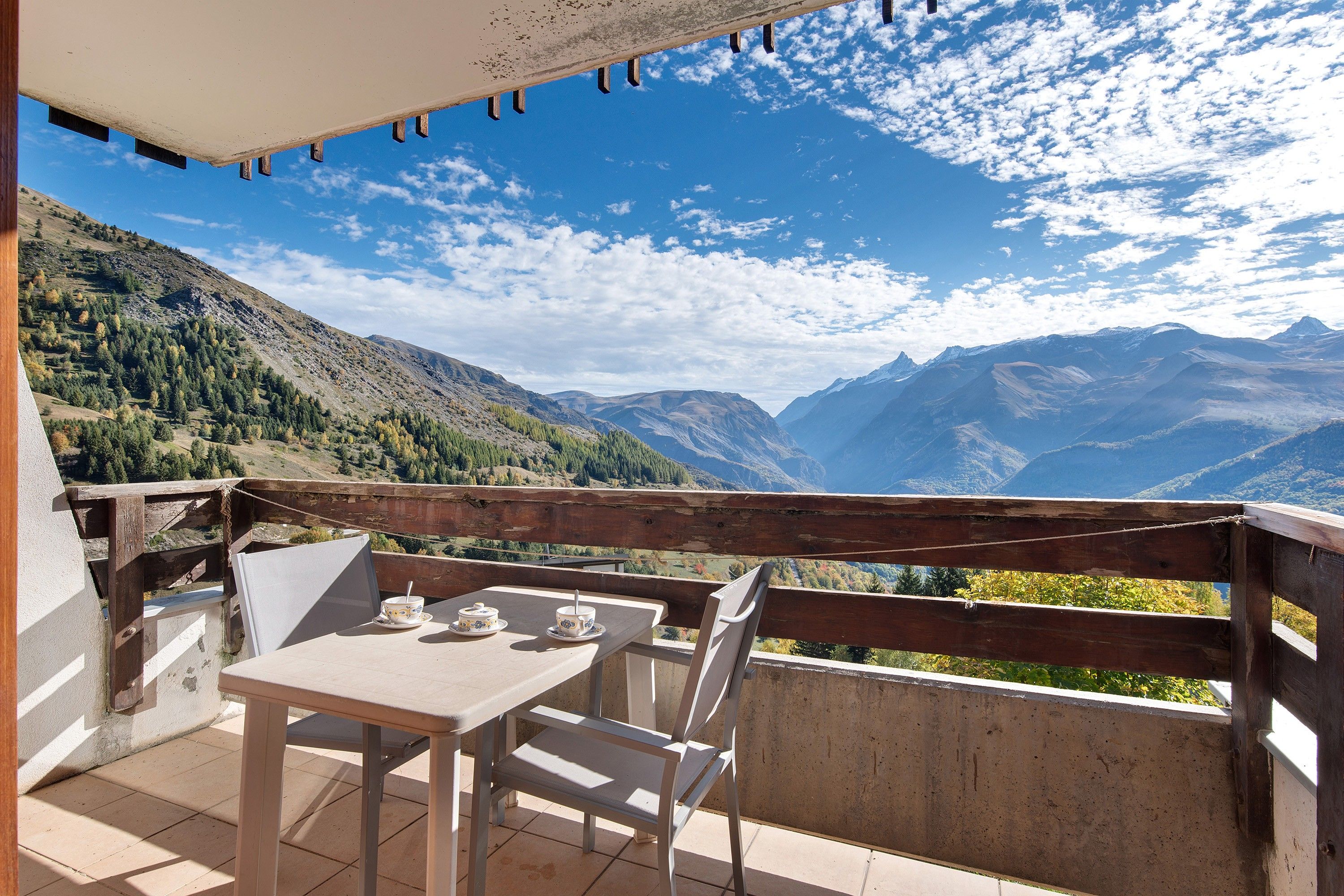 A terrace with a table and chairs, overlooking a mountainous landscape.