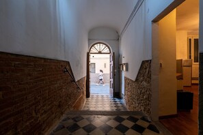 A hallway with a checkered floor, a brick wall on one side, and a white wall on the other.