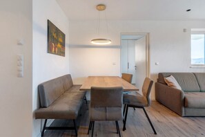 A modern living room with a wooden dining table, grey sofas, and a painting on the wall.