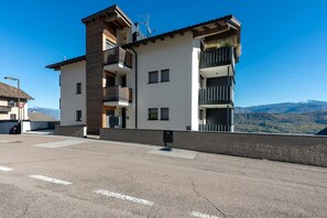 A modern multi-story building with balconies, a garage, and a clear view of mountains in the background.