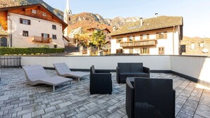 En takterrass med solstolar, ett stengolv och byggnader i bakgrunden.