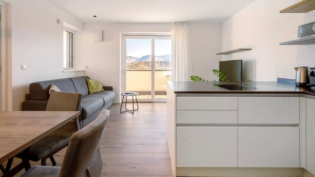 En modern lägenhet med matplats, soffa, kök och en stor skjutdörr i glas som leder ut till en balkong.