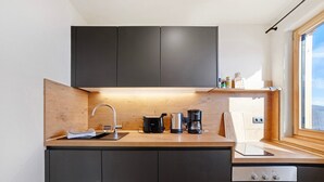 Una cocina moderna con armarios oscuros, encimera de madera, cafetera y hervidor.