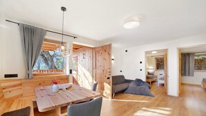 Un interior moderno con suelo de madera, una zona de comedor con mesa y sillas, un sofá y un ventanal con cortinas.