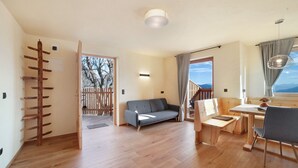 Un interior moderno con piso de madera, un sofá, una mesa de comedor con sillas y una escalera que lleva a un área exterior.