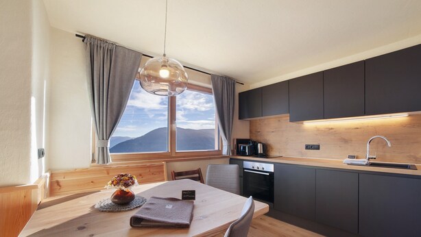 Una cocina moderna con una mesa y sillas de madera, vistas a montañas y un mueble oscuro.