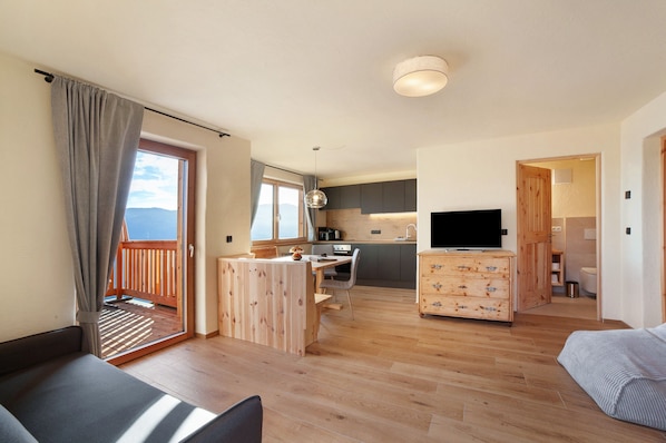 A modern living room with a wooden floor, a sofa, a TV, and a balcony with curtains.