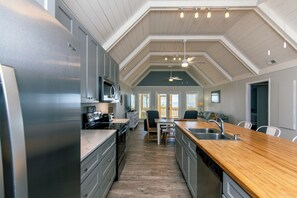 A modern kitchen with a wooden countertop, stainless steel appliances, and a high ceiling with exposed beams. - Barefoot Bungalow:Oceanfront Dog-friendly Home with Amazing Views,Sun Deck,Screened Porch & WiFi (Edisto Beach)