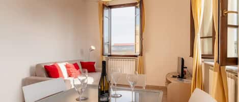 A modern living room with a glass table, a sofa with red cushions, a wine bottle, and glasses.
