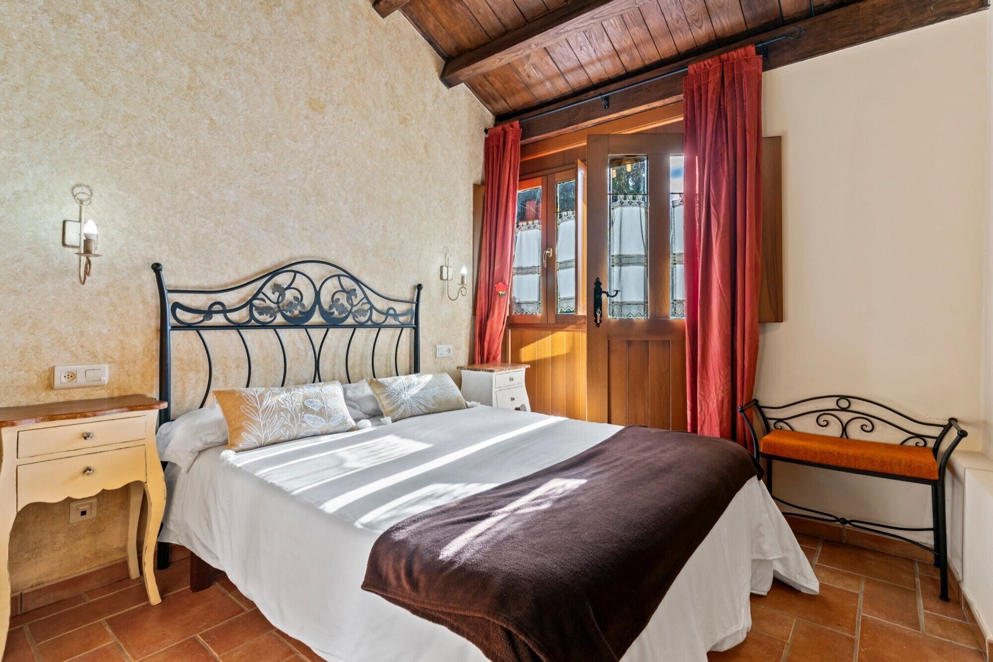 A bedroom with a bed, bedside table, nightstand, and a window with curtains.