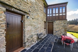A stone building with two wooden doors, a bench, and a table with a red tablecloth. - Country House 'Morouzos' with Shared Terrace, Shared Garden and Wi-Fi (Ortigueira)