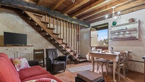 Un salon chaleureux avec un escalier en bois, une télévision, un canapé et un coin repas comprenant des chaises et une table.