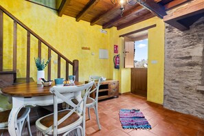 A dining area with a wooden table, white chairs, a colorful rug, a staircase, and a stone wall. - Country House 'Eiron' with Shared Terrace, Private Garden and Wi-Fi (ESPASANTE)