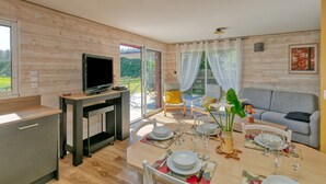 A modern kitchen with a flat-screen TV, wooden cabinets, and a dining area with a table set for four. - Holiday Home 'Gîte Le Champ Du Bois' with Private Terrace, Private Garden and Wi-Fi (Missillac)