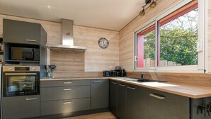 A modern kitchen with built-in appliances, a wooden countertop, and a window with a view of greenery. - Holiday Home 'Gîte Le Champ Du Bois' with Private Terrace, Private Garden and Wi-Fi (Missillac)