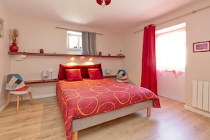 Une chambre à coucher comprenant un lit, une chaise, une étagère avec des objets décoratifs, une fenêtre avec des rideaux et un radiateur.