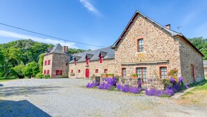 A stone building with multiple windows and doors, surrounded by gravel and purple flowers. - Holiday Home 'Gîte Le Champ Du Bois' with Private Terrace, Private Garden and Wi-Fi (Missillac)