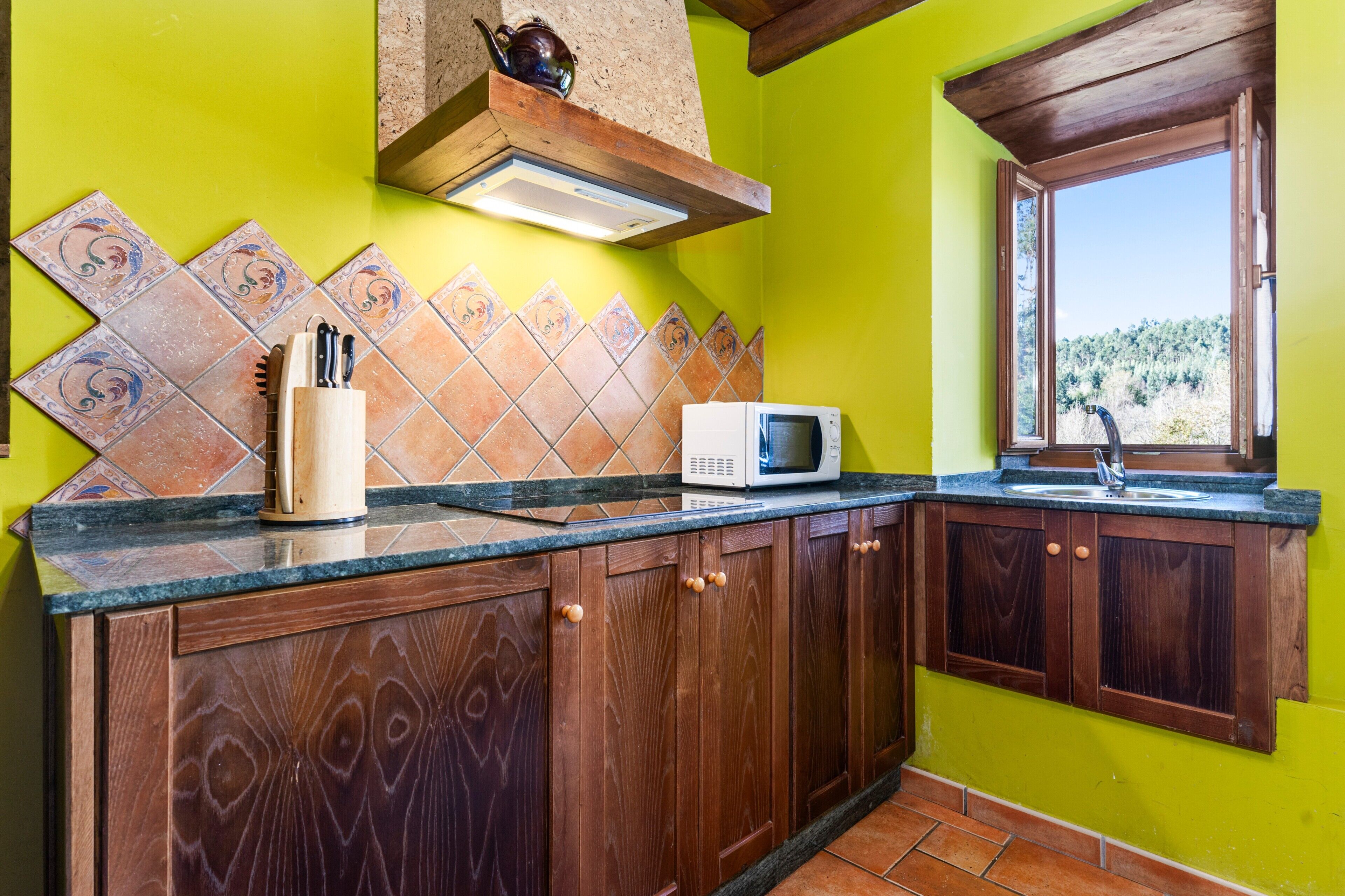 Una cocina con armarios de madera, microondas y ventana con vistas a árboles.