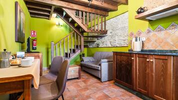 Une cuisine avec un escalier en bois, une table à manger avec des chaises, un canapé et un mur recouvert de carreaux.