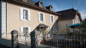 A two-story building with white shutters, a balcony, and a gated entrance. - La Maison Du Soleil - L'aulhère, Jacuzzi, Terrace, Air Conditioning, Sleeps 6 (Ledeuix)