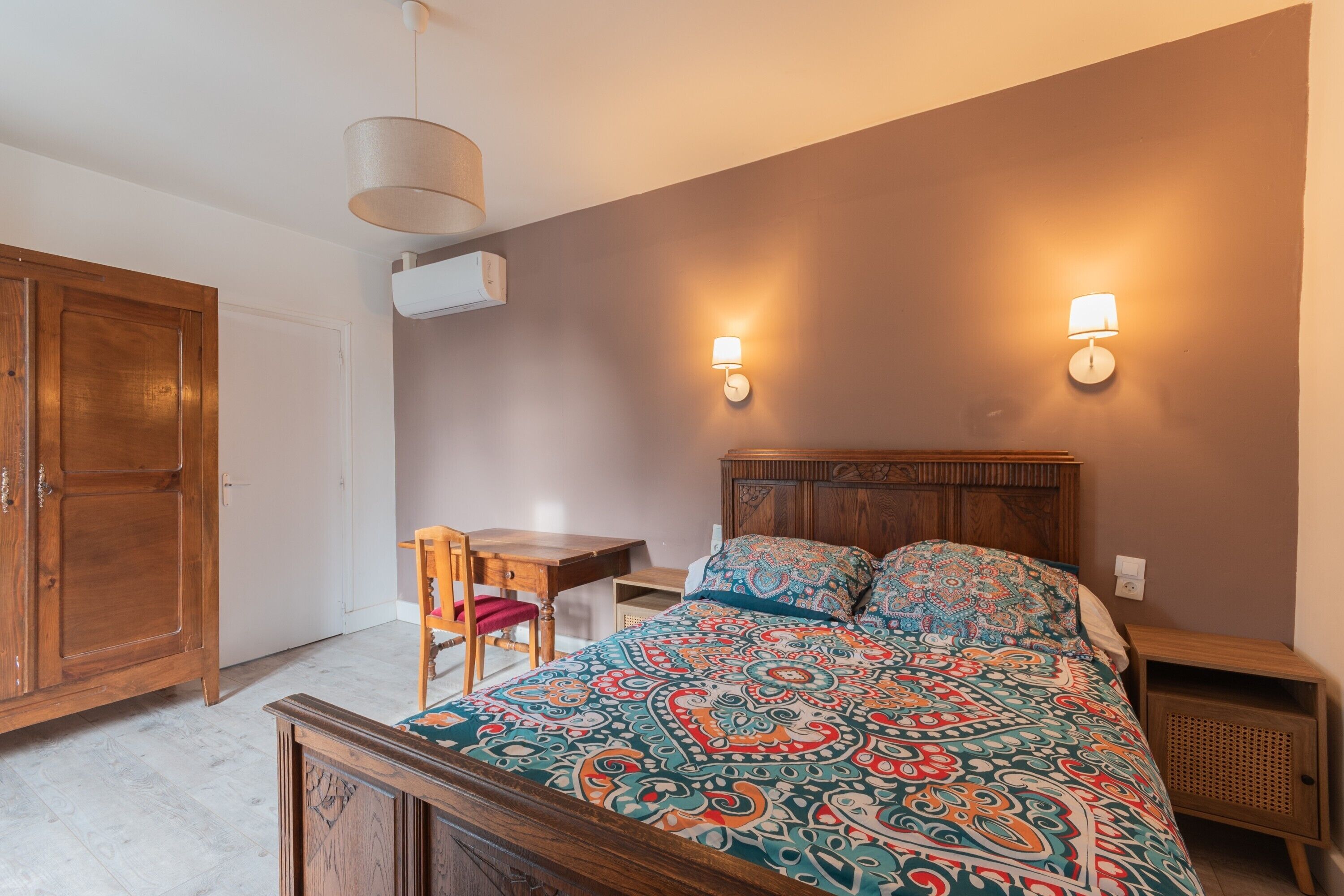 A bedroom with a wooden bed, two bedside lamps, a desk, and a chair.