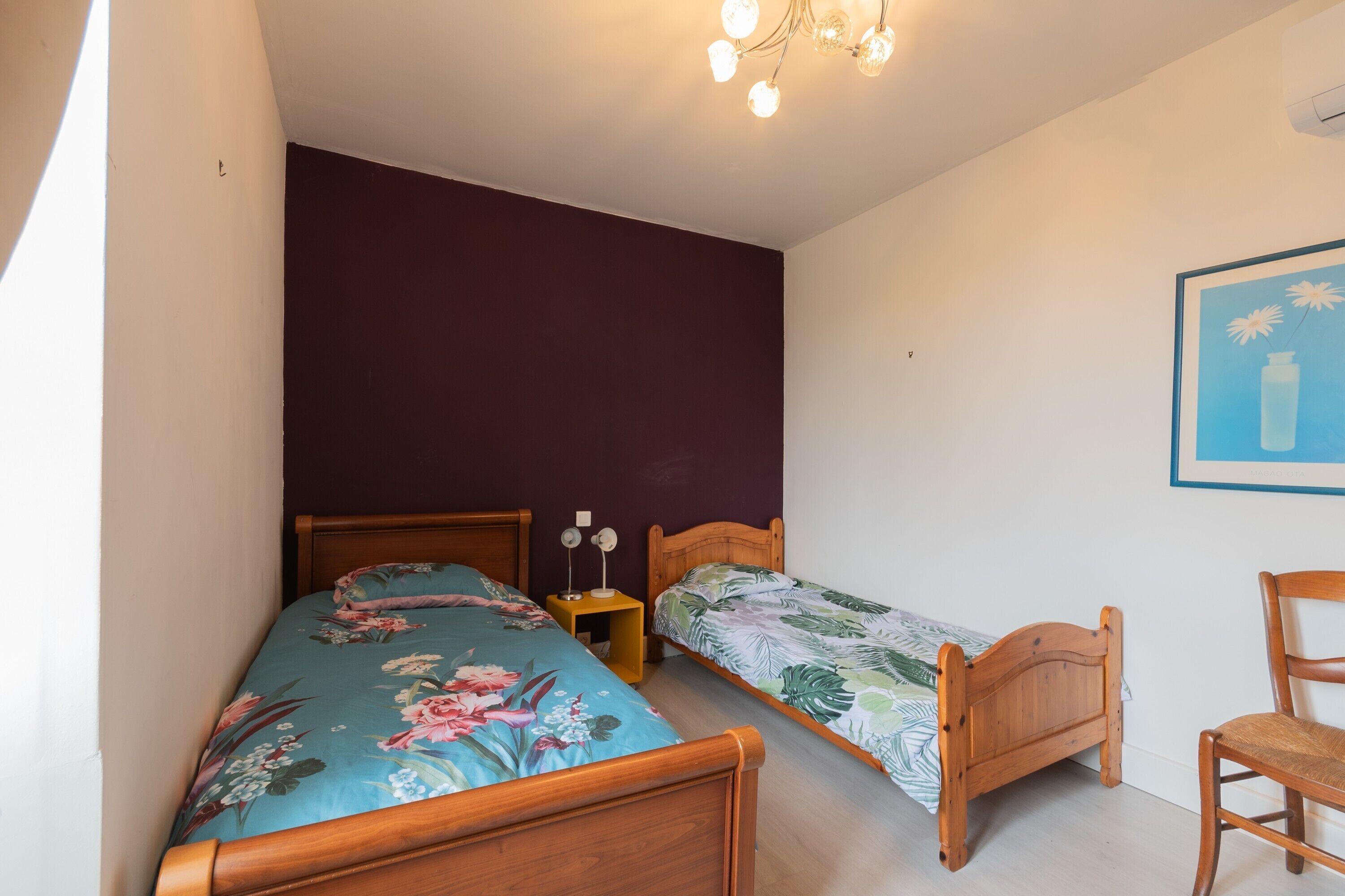 Ein Schlafzimmer mit zwei hölzernen Betten, einem Nachttisch mit Lampen, einem Sessel und einem gerahmten Bild an der Wand.