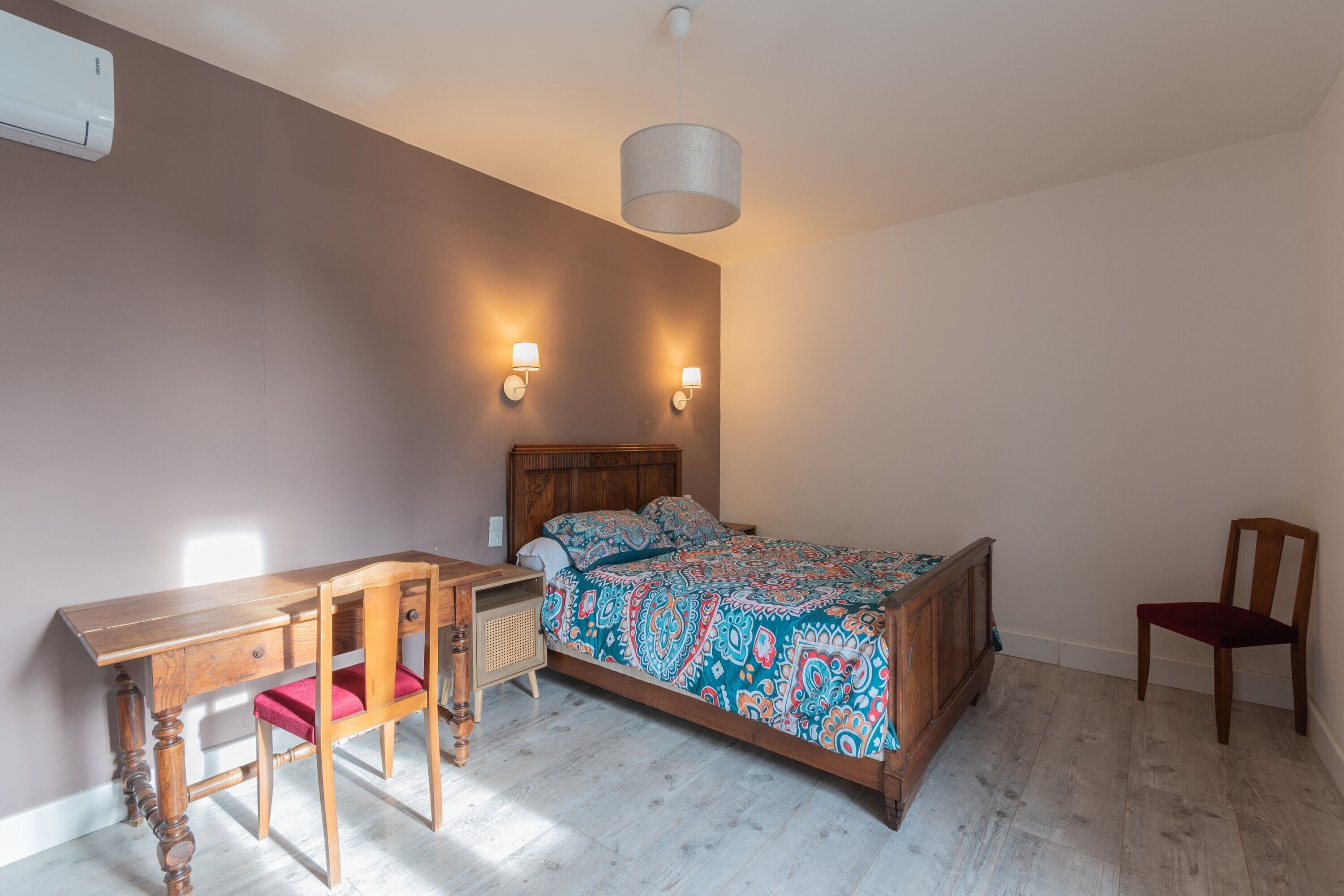 Un dormitorio con una cama de madera, un escritorio, una silla y dos lámparas fijadas a la pared.