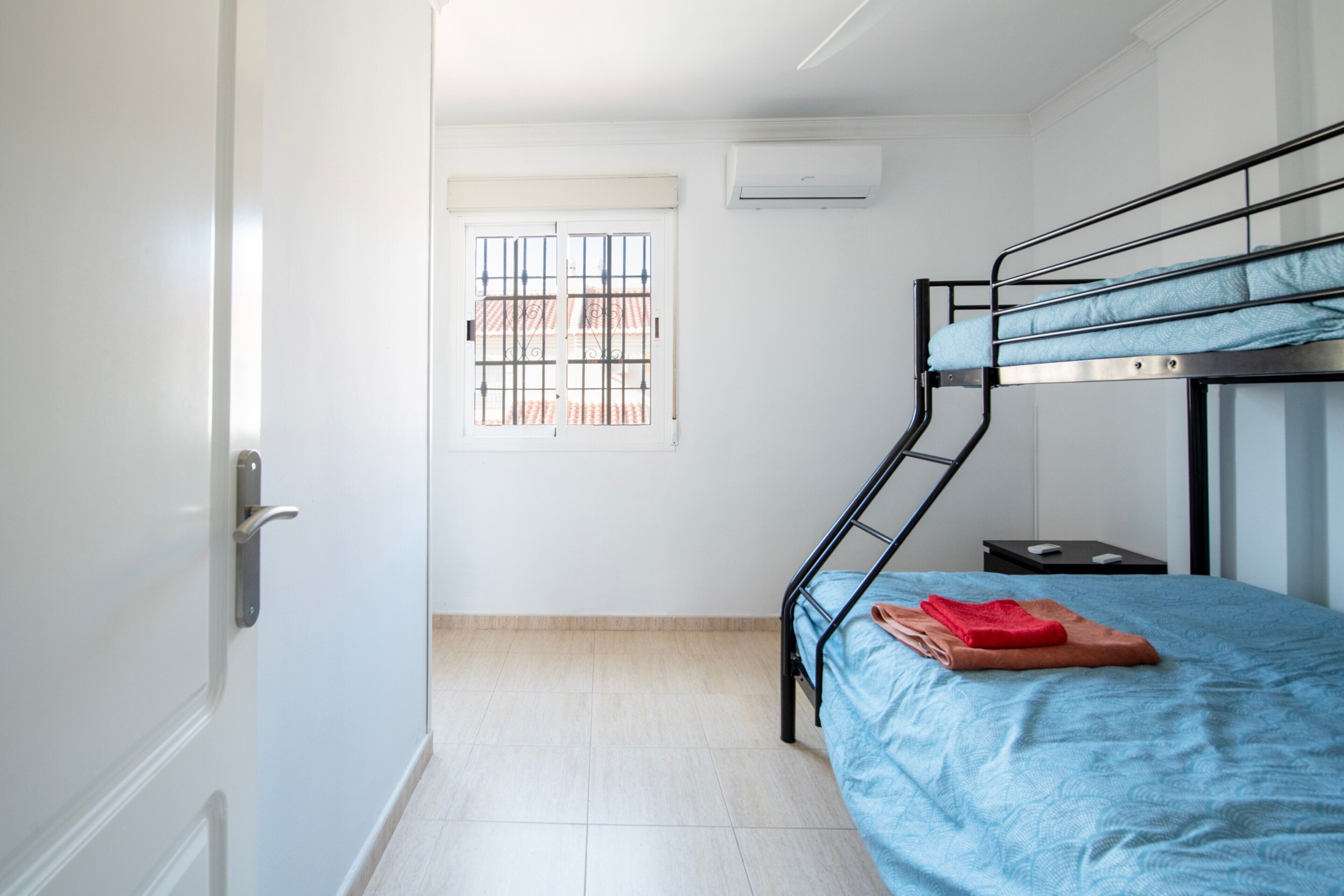 A bunk bed room with a window, a door, and a small bedside table.