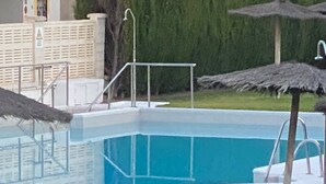Una piscina con una escalera metálica, una sombrilla de paja y una valla de madera.