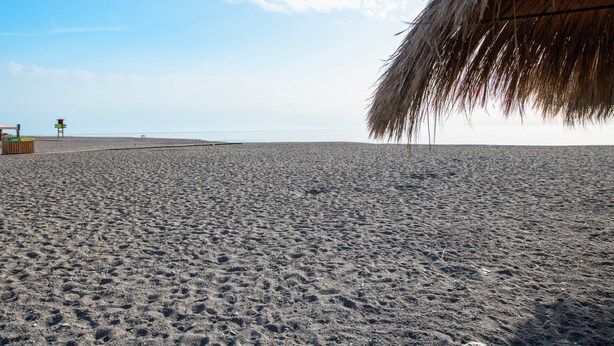 Una playa con una estructura de techo de paja, una torre de salvavidas y un camino de arena.