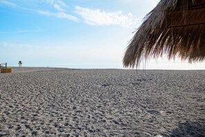 A beach with a thatched structure, a lifeguard tower, and a sandy path.