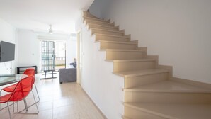 Una escalera que lleva a un piso superior, un comedor con sillas rojas y un televisor en la pared.