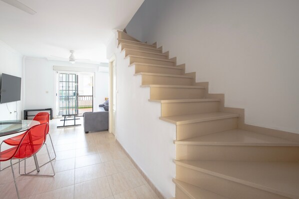 A staircase leading to an upper floor, a dining area with red chairs, and a television on the wall.
