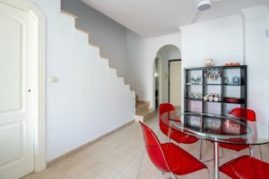 A dining area with a glass table and red chairs, a staircase, and a kitchen area with shelves.