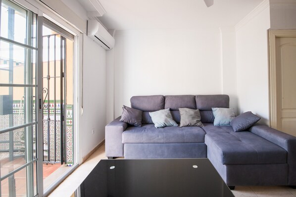 Ein Wohnzimmer mit grauem Sofa, einem schwarzen Couchtisch und einer Schiebeglastür, die zu einem Außenbereich führt.