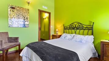 Una habitación con una cama, una silla, un cuadro en la pared, una puerta y una mesita de noche con una lámpara.