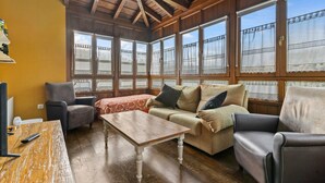 A cozy room with wooden beams, large windows with lace curtains, a sofa, a table, and a chair. - Country House 'A Concha' with Shared Terrace, Private Garden and Wi-Fi (ESPASANTE)