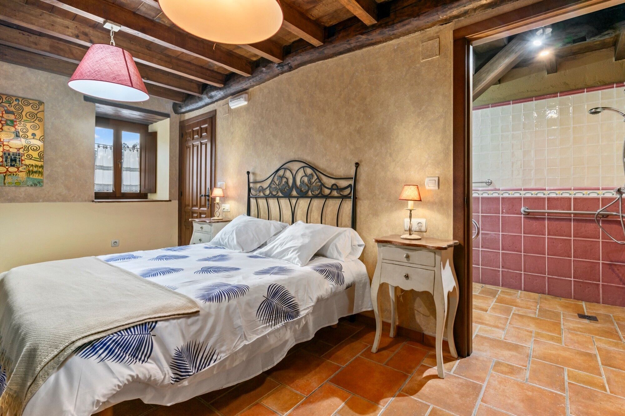 A bedroom with a bed, bedside tables, a window, and a bathroom with a tiled wall and shower.
