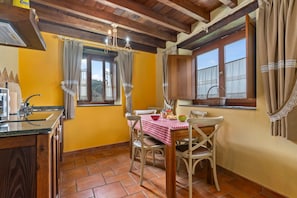 A kitchen with a table and chairs, a window with curtains, and a wooden ceiling. - Country House 'A Concha' with Shared Terrace, Private Garden and Wi-Fi (ESPASANTE)