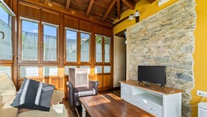 A cozy living room with a stone wall, wooden furniture, and a television. - Country House 'A Concha' with Shared Terrace, Private Garden and Wi-Fi (ESPASANTE)