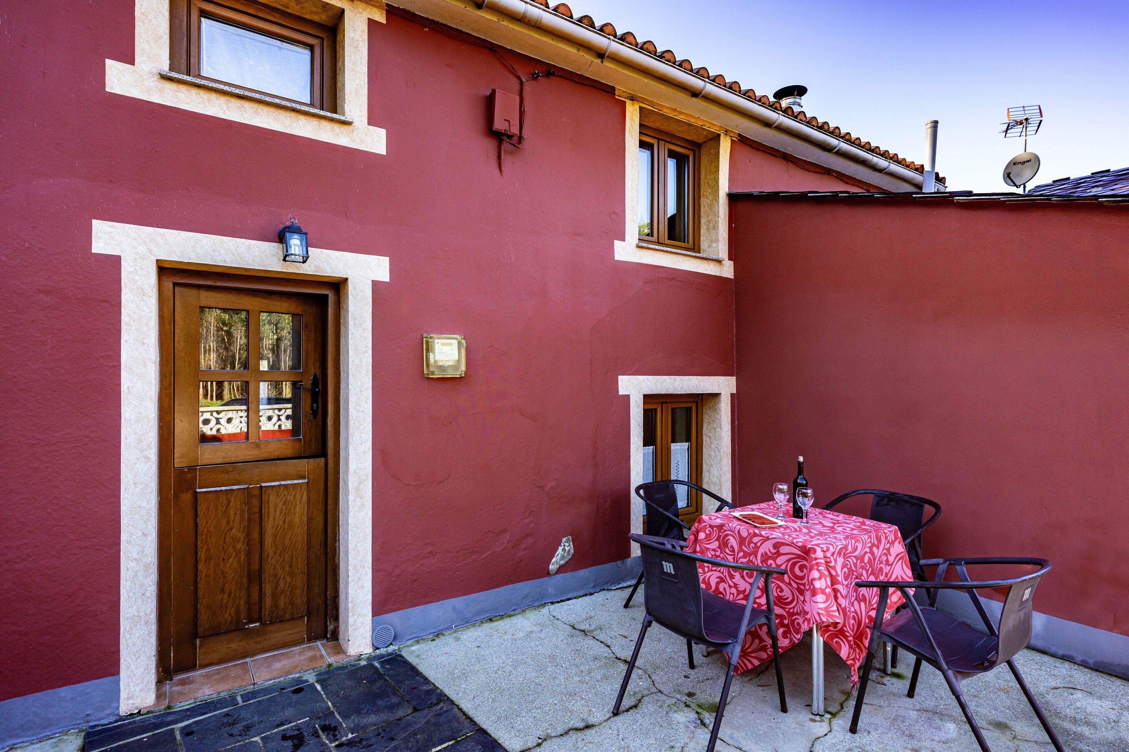 Un edificio rojo con una puerta de madera, una ventana y una mesa con sillas afuera.