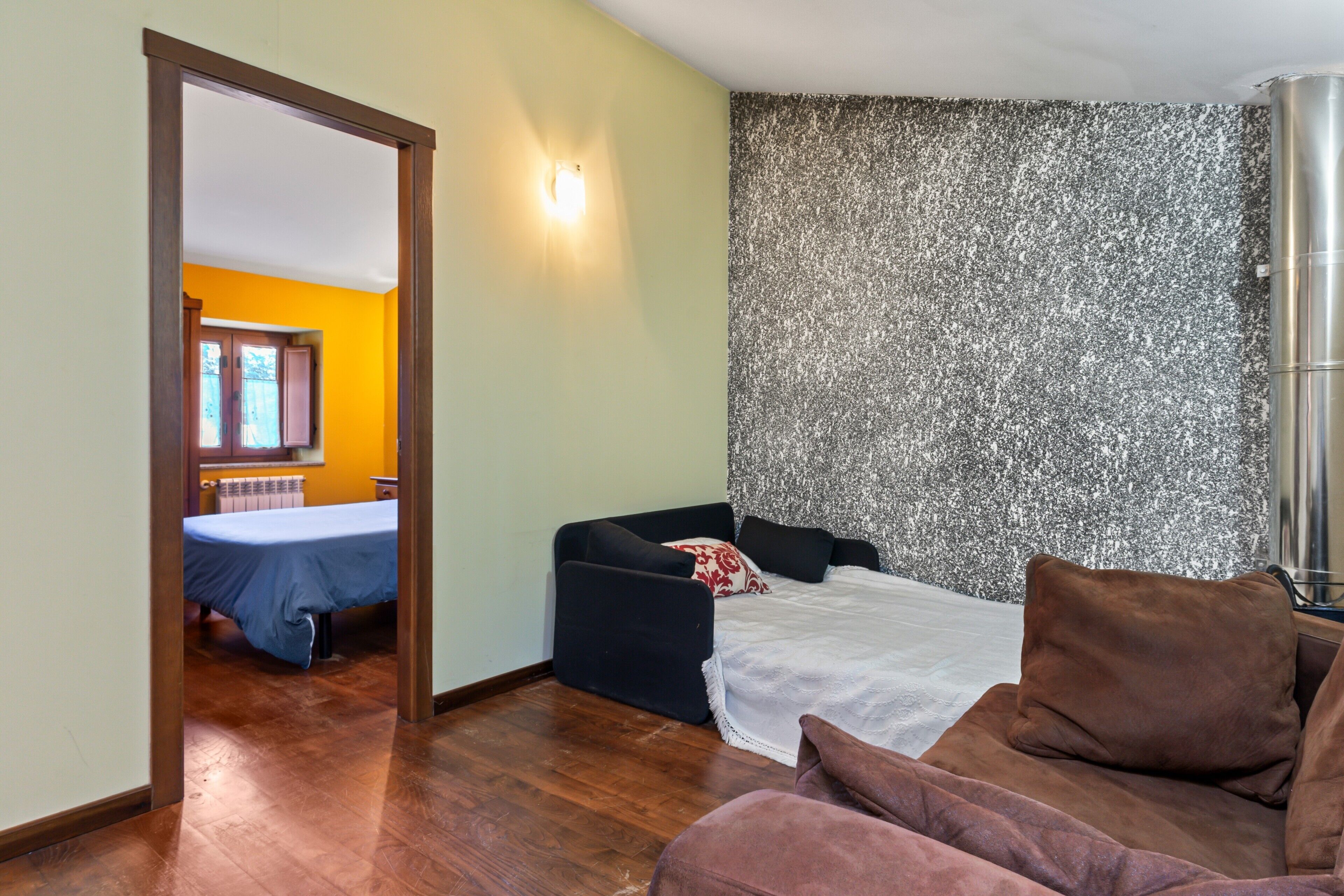 A room with a bed, a sofa, a small table, and a wall with a textured pattern.