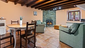 Una sala de estar acogedora con chimenea de piedra, vigas de madera, una mesa de comedor con sillas y un sofá verde.
